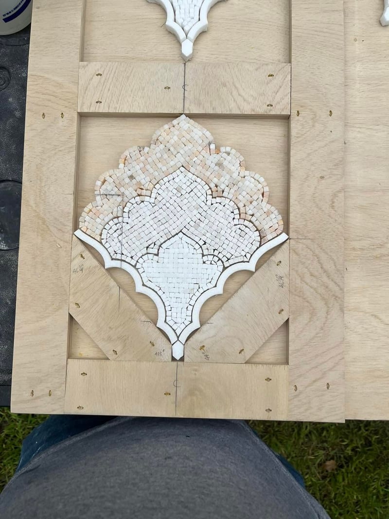 Hand-assembled marble mosaic panel laid out on a wooden jig at the workbench